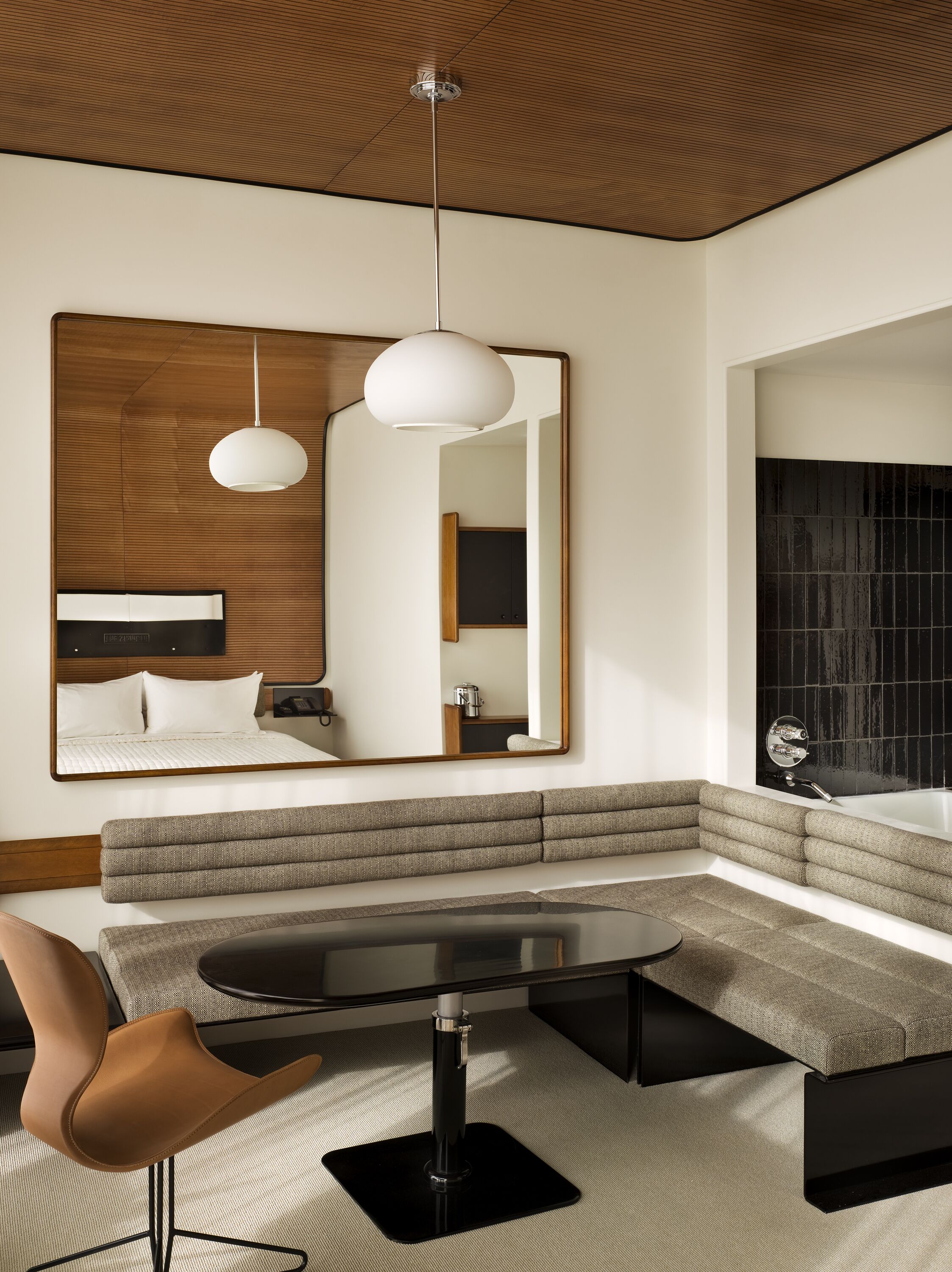 A modern hotel room with a large bed, a seating area with a sofa and armchairs, a dining table, and a large mirror.