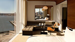 Une chambre d’hôtel moderne dotée d’une grande fenêtre donnant sur la ville, d’un coin salon confortable et d’un espace repas.