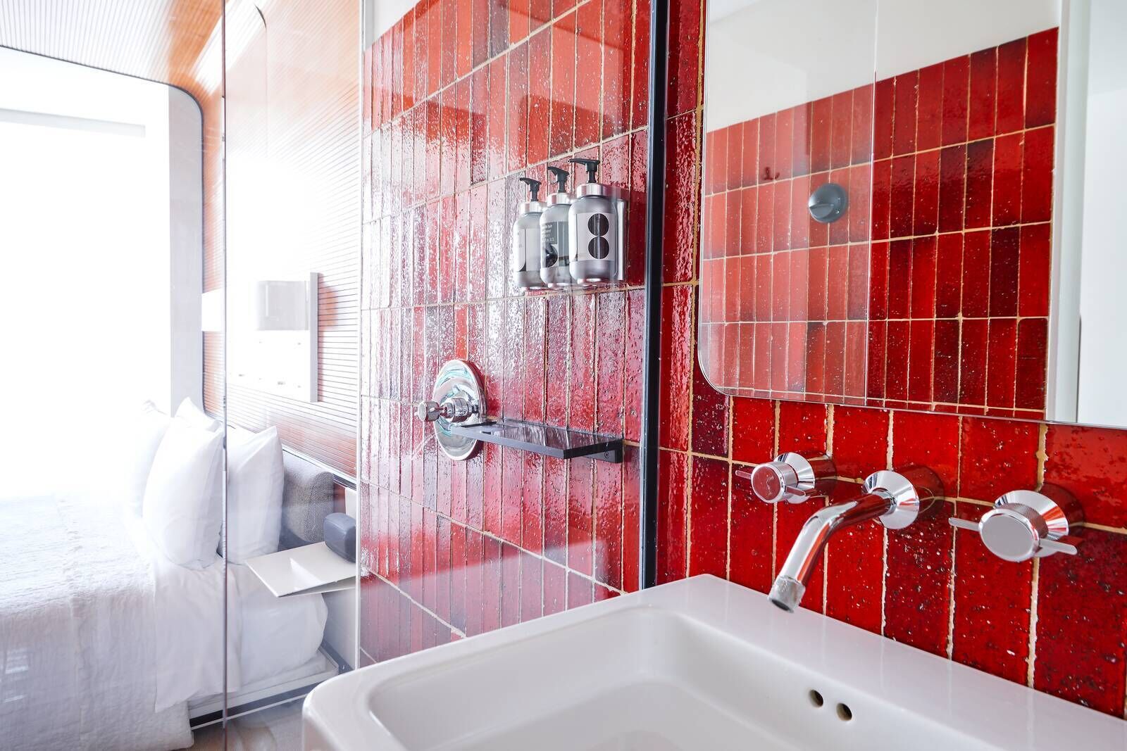 A bathroom with a white sink, red tiled walls, and a glass shower enclosure.