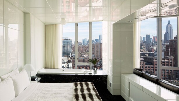 A modern bedroom with a large bed, a view of the cityscape, and a window with a curtain. - The Standard High Line (New York)