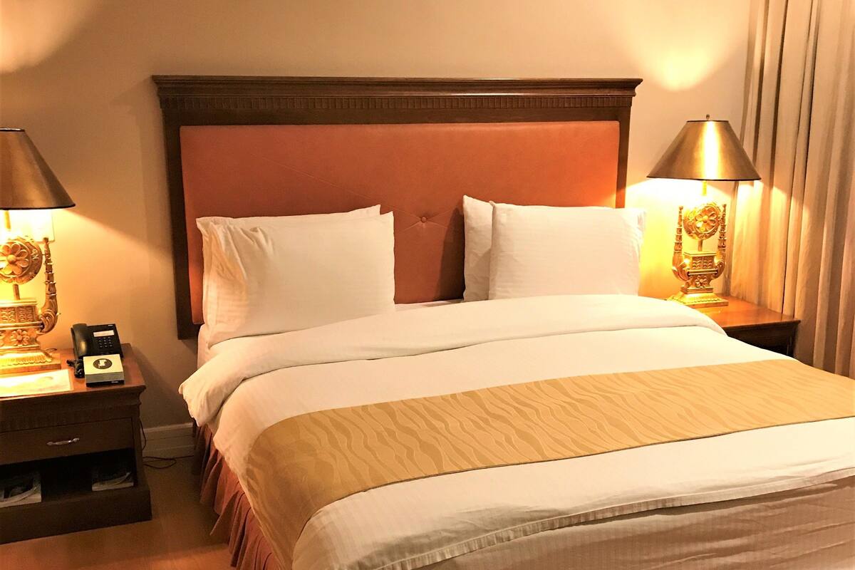 Une chambre d’hôtel avec un grand lit, deux tables de chevet et une petite table d’appoint.