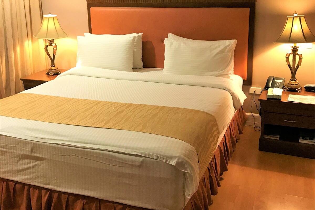 Une chambre d’hôtel avec un grand lit, deux lampes de chevet, une table de chevet avec un téléphone et une tête de lit en bois.