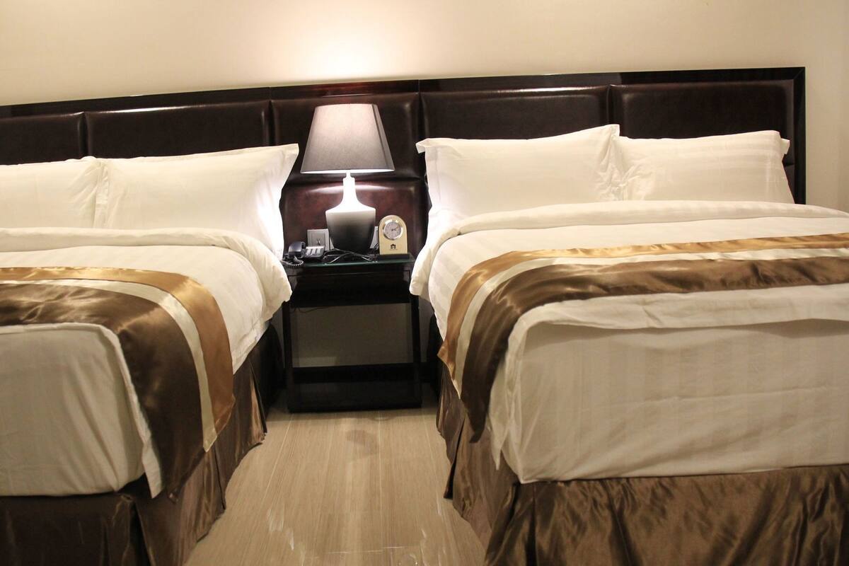Une chambre d’hôtel avec deux lits, une table de chevet, une lampe et une horloge.