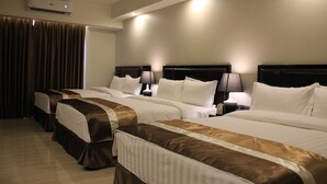 Ein Hotelzimmer mit vier Betten, jeweils mit Kopfteil, Nachttischen und Lampen.