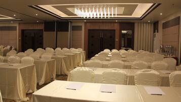 A conference room with rows of tables covered in white tablecloths and chairs, a chandelier, and a modern ceiling design.