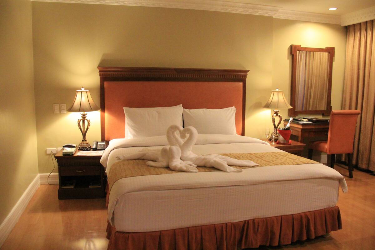Une chambre d’hôtel avec un grand lit, deux tables de chevet, un bureau avec une chaise et une fenêtre avec des rideaux.