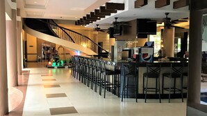 Eine geräumige Lobby mit einer zentralen Treppe, einer Bar mit Sitzgelegenheiten und einem Fliesenboden.