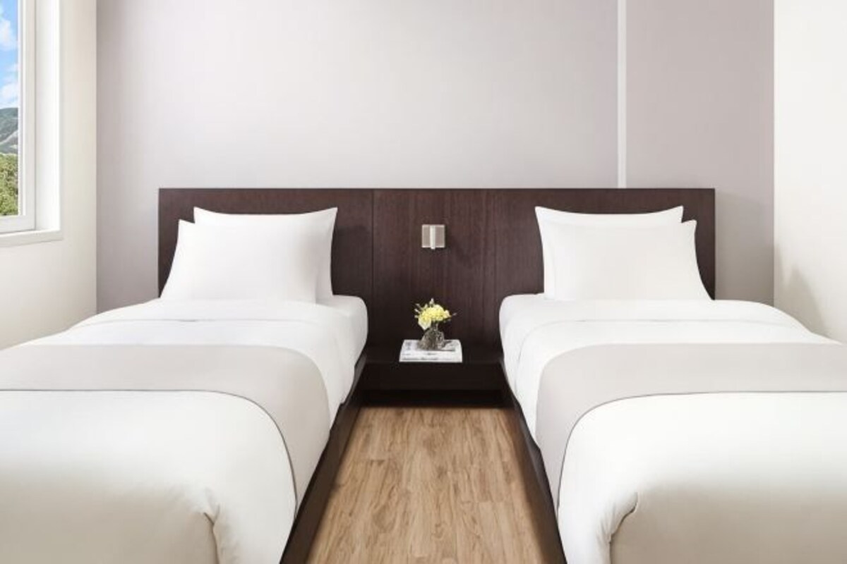 A double room with two beds, a wooden floor, and a small table with a vase.