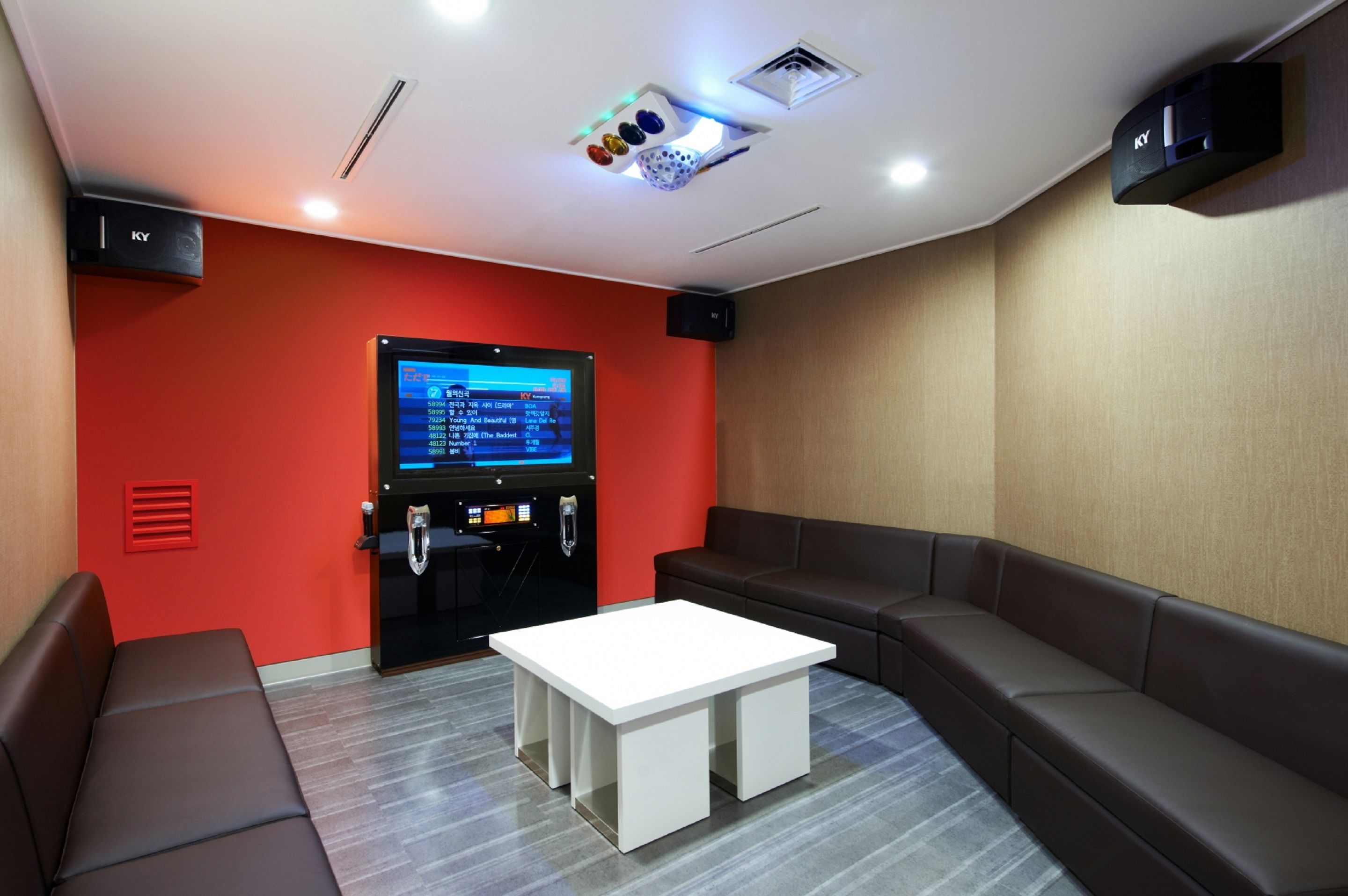 A modern room with a red accent wall, a large screen, a white table, and a brown sofa.