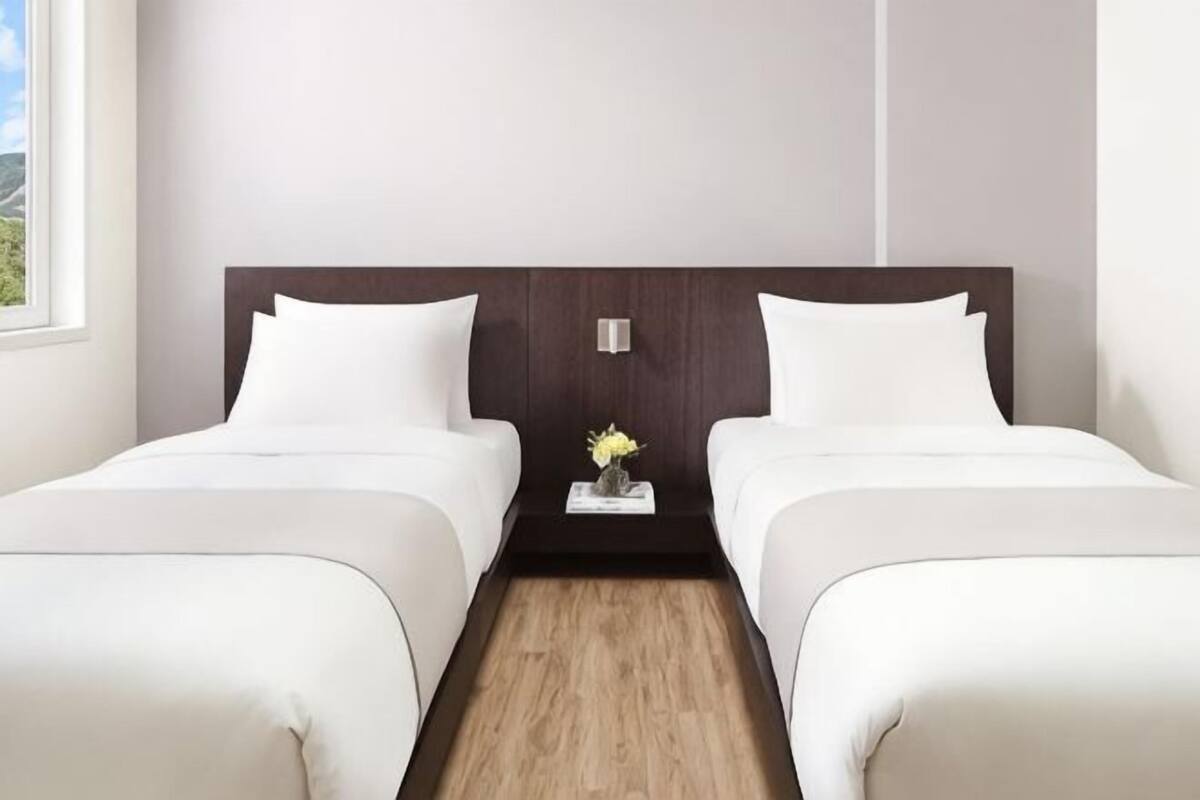 A double room with two beds, a wooden floor, and a small table with a vase.