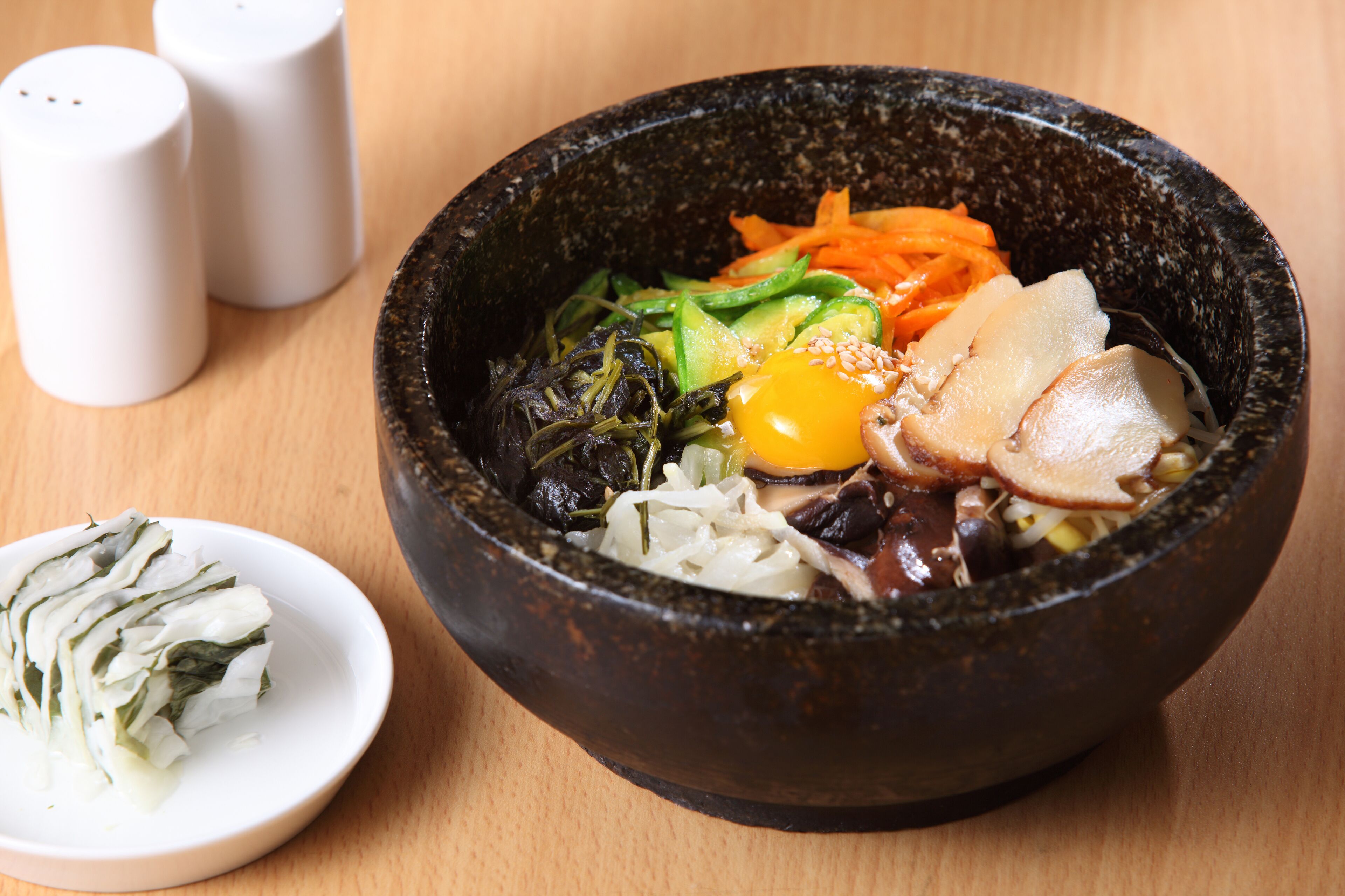 A bowl of food with various vegetables and a boiled egg on a wooden table.