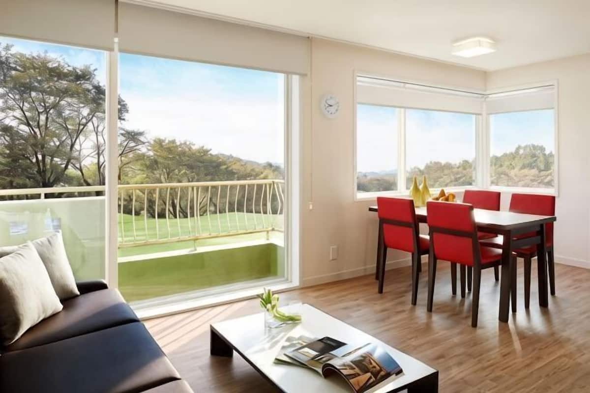 A modern living room with a balcony, a dining area, and large windows.