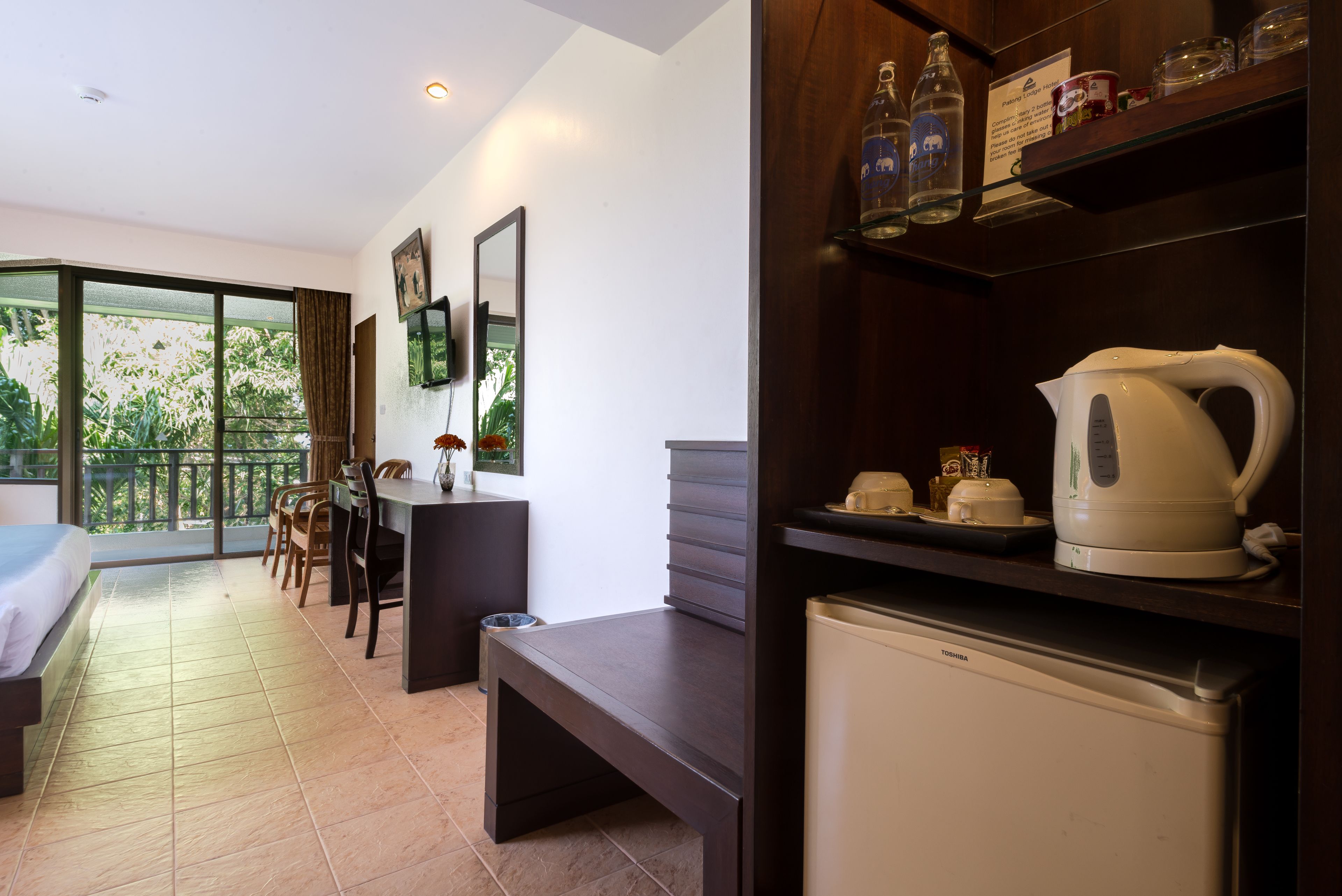 Une chambre d’hôtel moderne dotée d’un balcon, d’un coin repas, d’un canapé, d’un réfrigérateur et d’une machine à café.