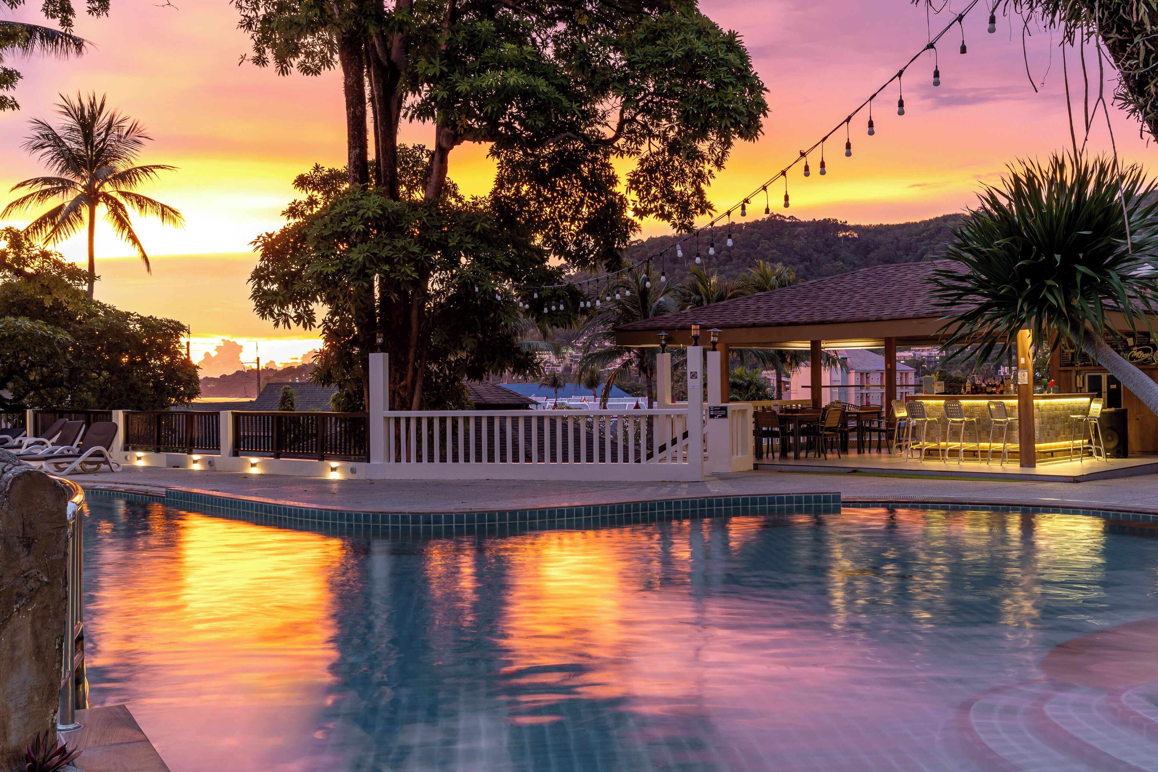 A pool area with a sunset view, lounge chairs, and a bar area.
