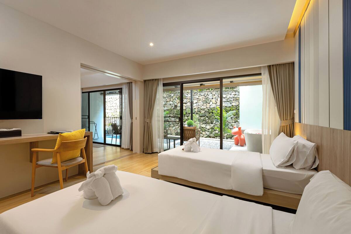 A hotel room with two beds, a desk, a chair, and a TV.