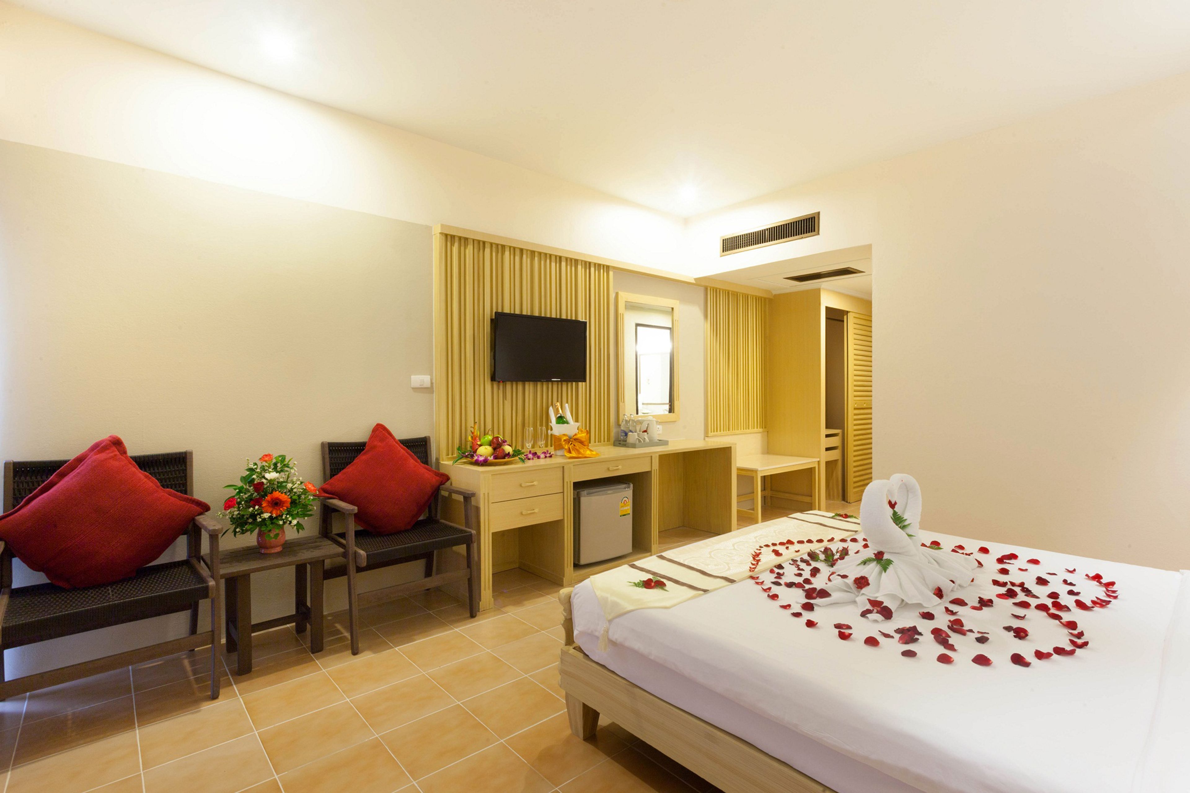 A hotel room with a bed, a desk, a chair, a TV, and a small table with a flower arrangement.