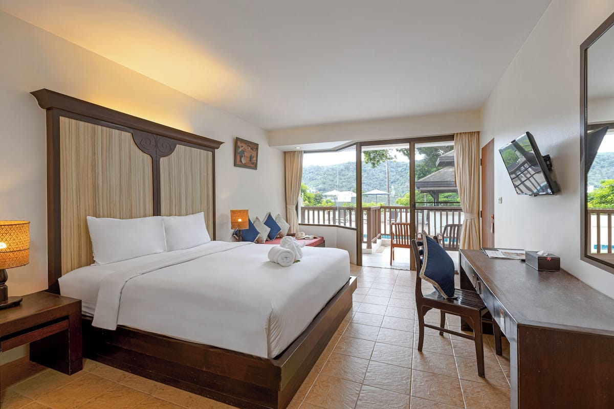 A hotel room with a large bed, a desk, and a balcony with a view of the mountains.