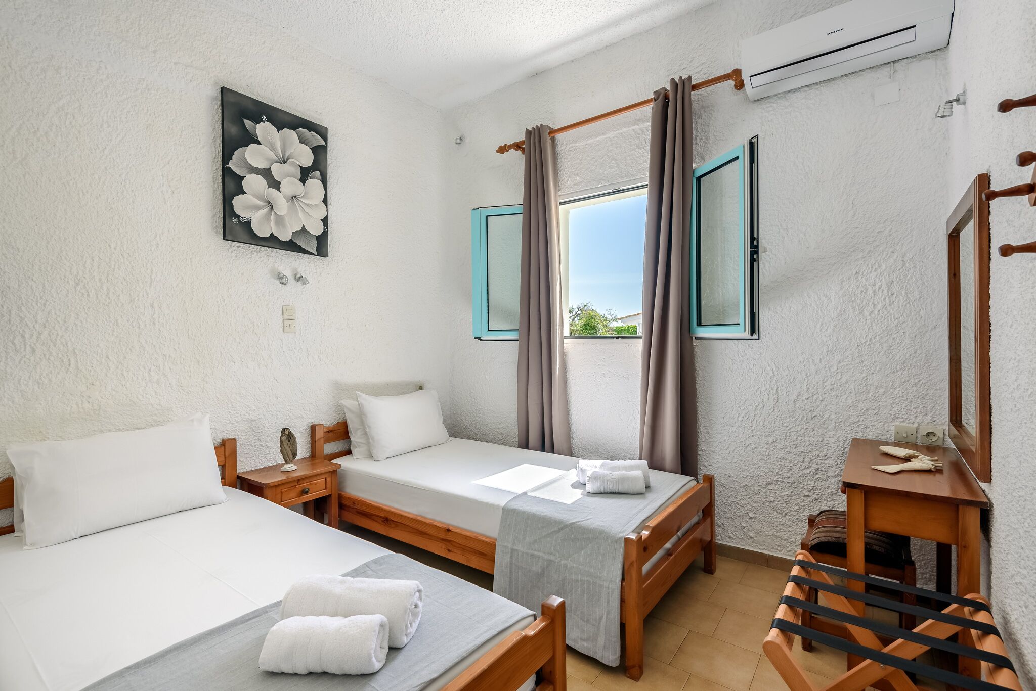A room with two single beds, a wooden chair, a small table, and a window with curtains.