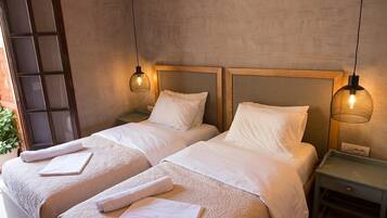 Habitación de hotel con dos camas, cada una con cabecero de madera, ropa de cama blanca y una mesita de noche con lámpara.