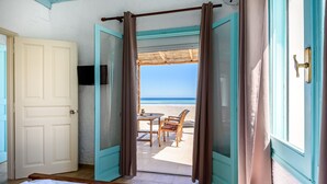 Una habitación con cama, televisión y vistas a la playa a través de cortinas abiertas.