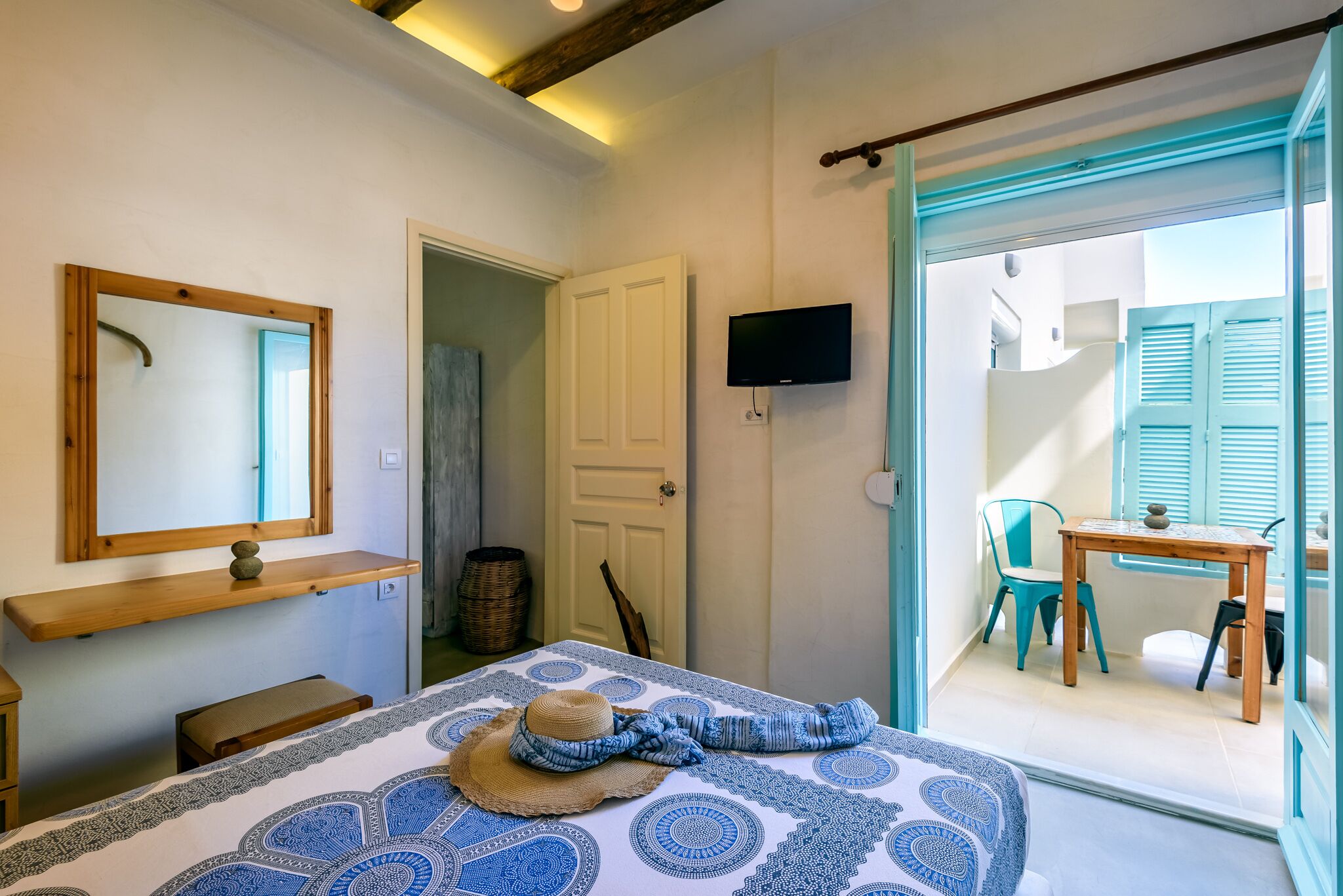 A bedroom with a bed, a wooden shelf, a television, and a view of an outdoor balcony with a table and chairs.