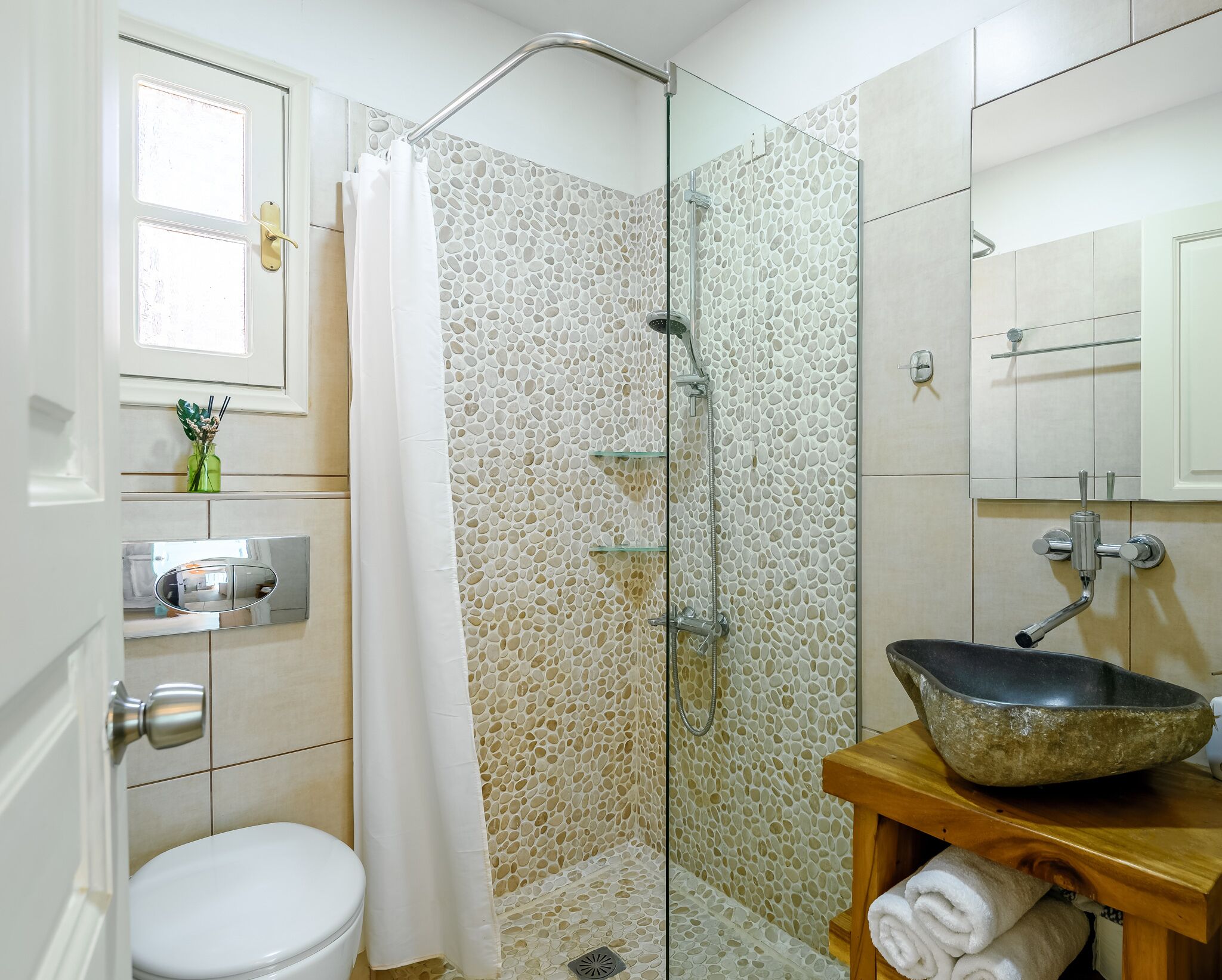 A bathroom with a glass-enclosed shower, a white toilet, a wooden vanity with a stone basin, and a mirror above the sink.