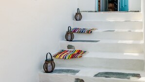 Un edificio blanco con una escalera que conduce a una puerta con marco azul. Hay almohadas coloridas y una cesta tejida en los escalones.