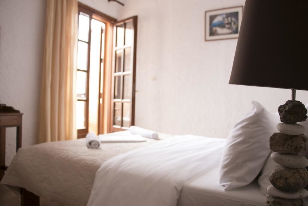 A neatly made bed with white linens, a lamp with a black shade, and a stack of stones beside it.