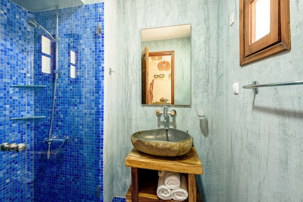 Un baño con pared de ducha de mosaico azul, tocador de madera con lavabo y espejo sobre el lavabo.