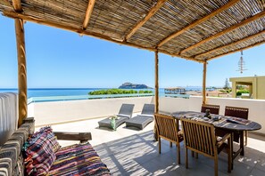 A covered outdoor seating area with a view of the sea and a distant mountain. - Ilias Apartments (Platanias)