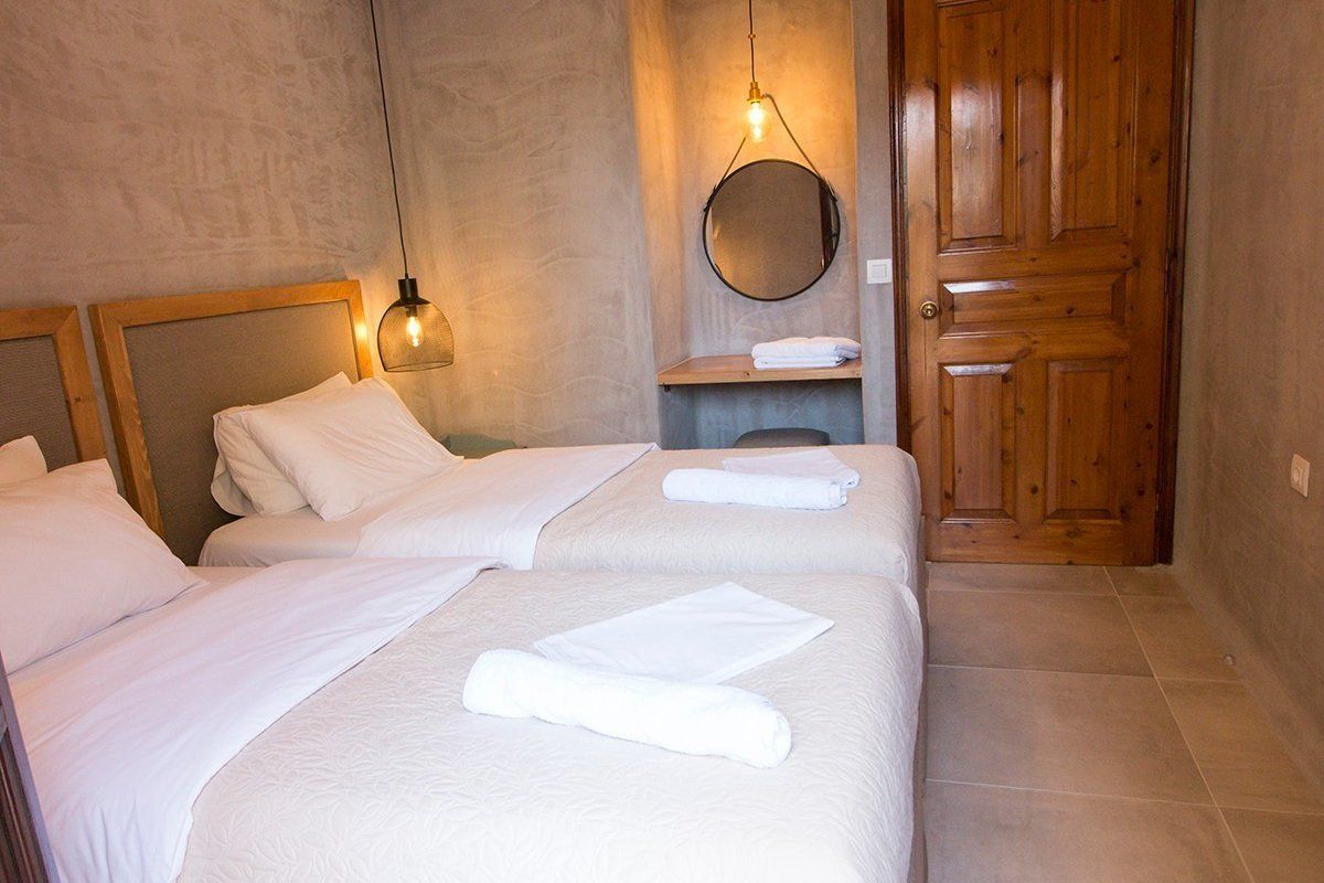 A hotel room with two beds, a wooden door, a round mirror, and a shelf with towels.