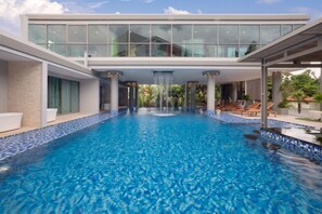 Un hotel moderno con una amplia piscina interior, un área cubierta con sillones de descanso y un nivel superior con techo de vidrio.