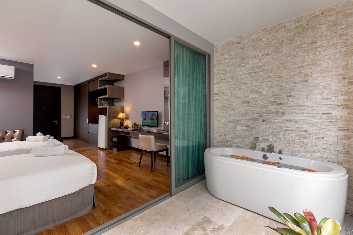 Une chambre d’hôtel moderne dotée d’un grand lit, d’un espace bureau séparé, d’une baignoire décorée de pétales de fleurs et d’un mur au motif de briques.