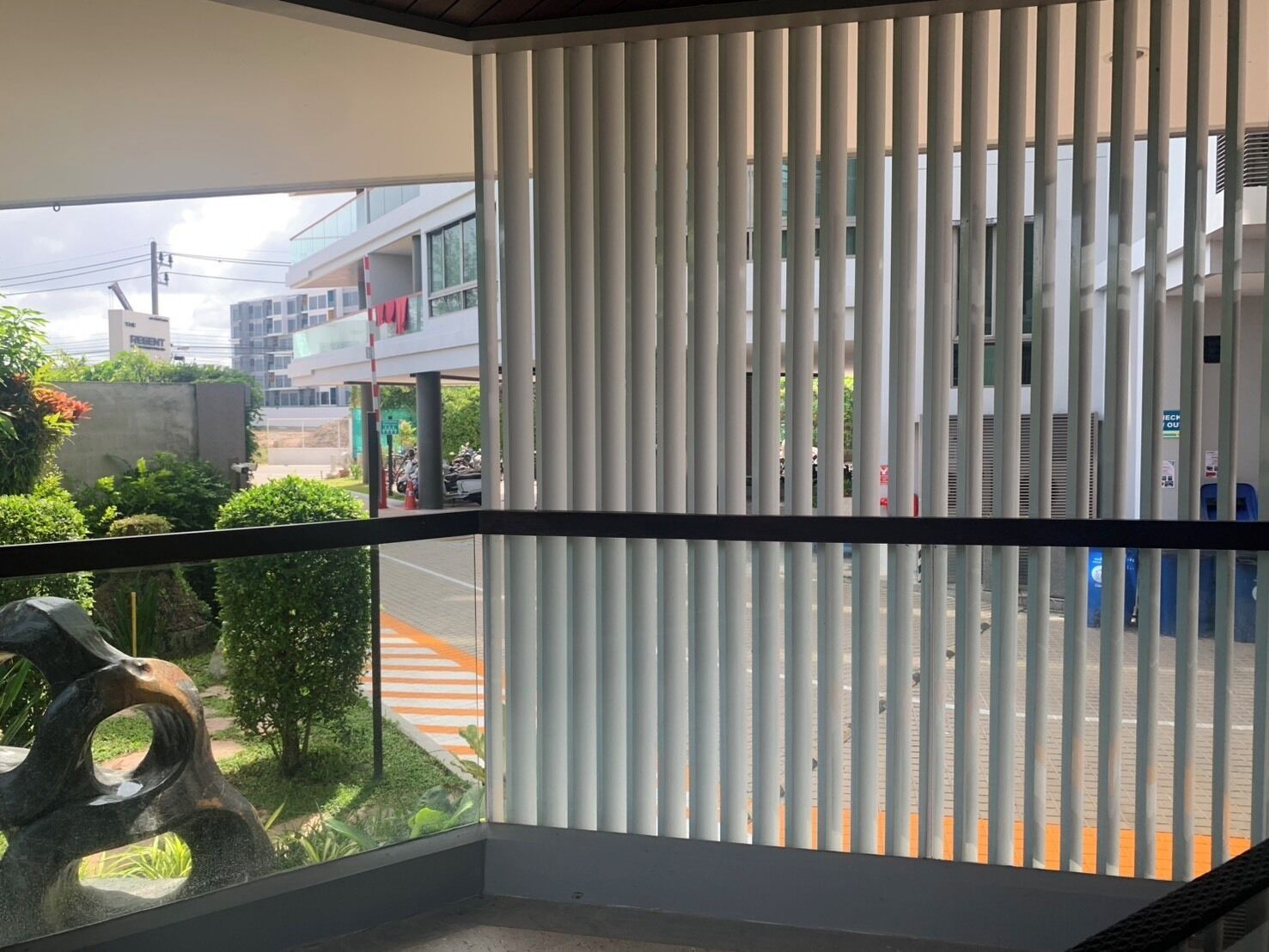 Un balcón con persianas verticales, vista a una calle con motocicletas estacionadas y un edificio con un cartel que dice 'Present'.