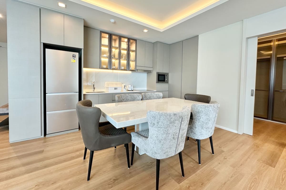 Une cuisine moderne dotée d’un îlot central, d’appareils électroménagers intégrés et d’un coin repas avec une table blanche et des chaises grises.