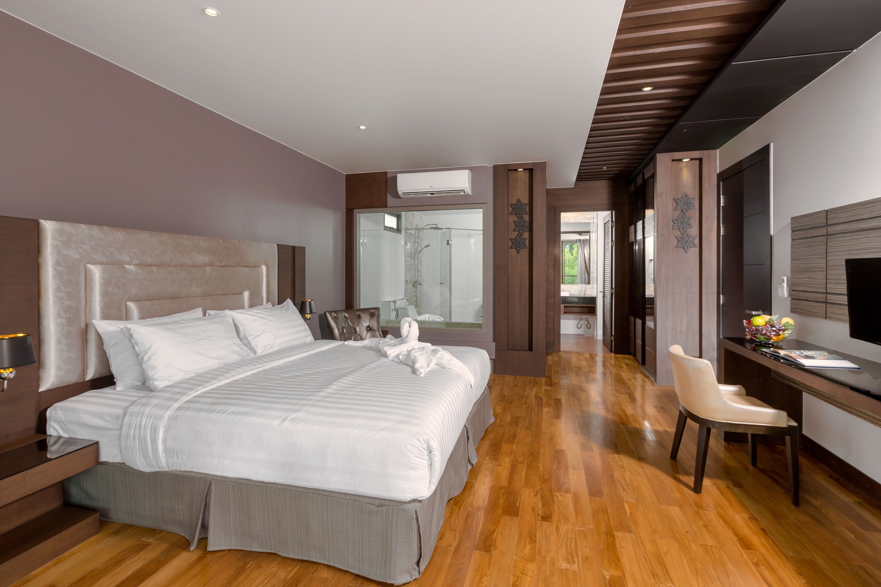 Una habitación de hotel moderna con una cama grande, un escritorio con silla, televisión y baño con ducha de vidrio.