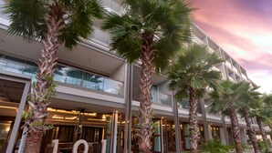 Ein modernes Hotel mit mehreren Etagen, großen Fenstern und Palmen im Vordergrund.