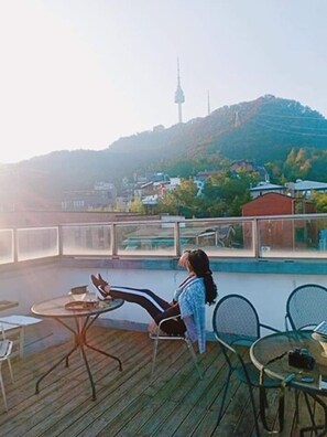 A person sitting on a deck chair overlooking a pool, with a view of a hill and a tower in the distance. - Namsan Guesthouse (Seoul)