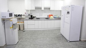 Una cocina compacta con gabinetes blancos, microondas, cafetera y refrigerador.