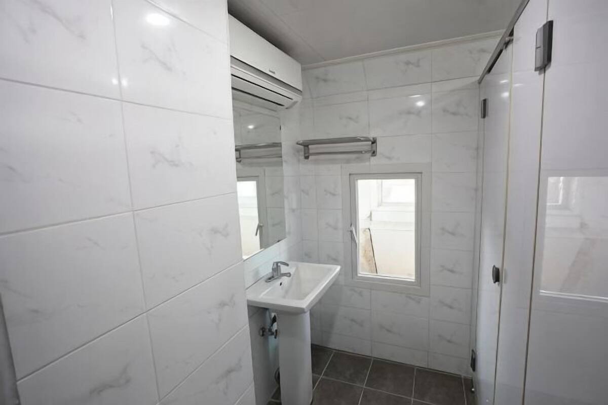 Un baño con azulejos de mármol blanco, un lavabo, un espejo y una ventana.