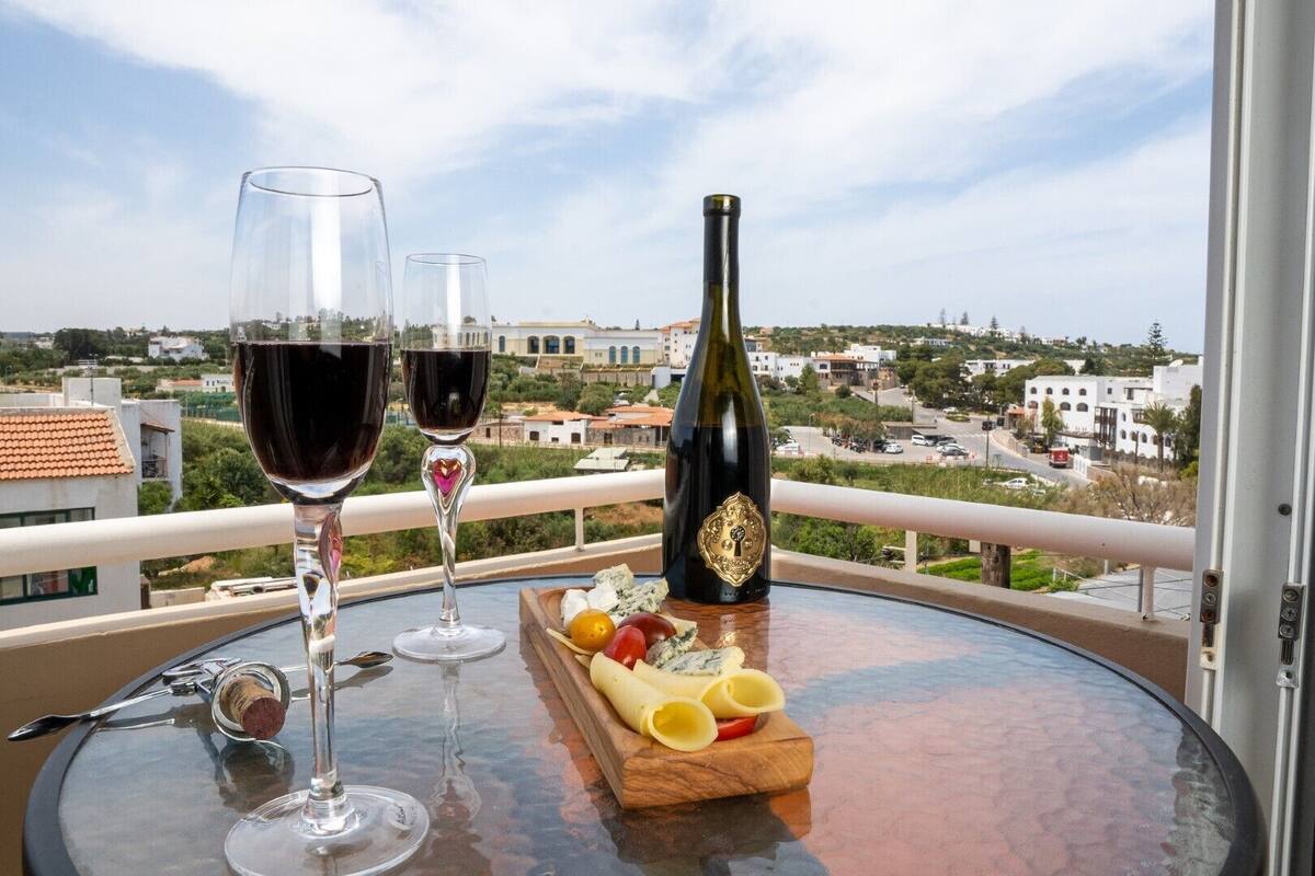 Ein Balkon mit zwei Weingläsern, einer Flasche und einem Holzboden mit Käse und Obst.