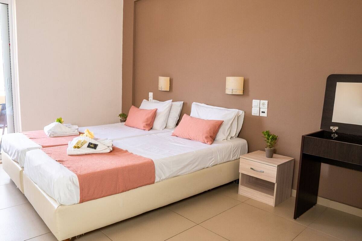 Ein Hotelzimmer mit zwei Betten, einem Nachttisch, einem Schreibtisch mit Spiegel und einer kleinen Topfpflanze.