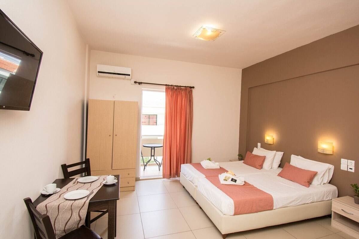 Ein Hotelzimmer mit Bett, Nachttischen, einem Schreibtisch mit Stühlen, einem Fernseher, einer Klimaanlage und einem Fenster mit Vorhängen.