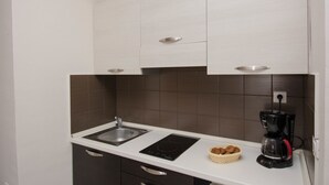 Una cocina compacta con un lavamanos, una placa de inducción negra y una cafetera.