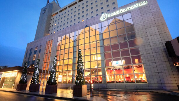 A hotel building with a large glass facade, a prominent 'Hotel Buena Vista' sign, and two Christmas trees in front.