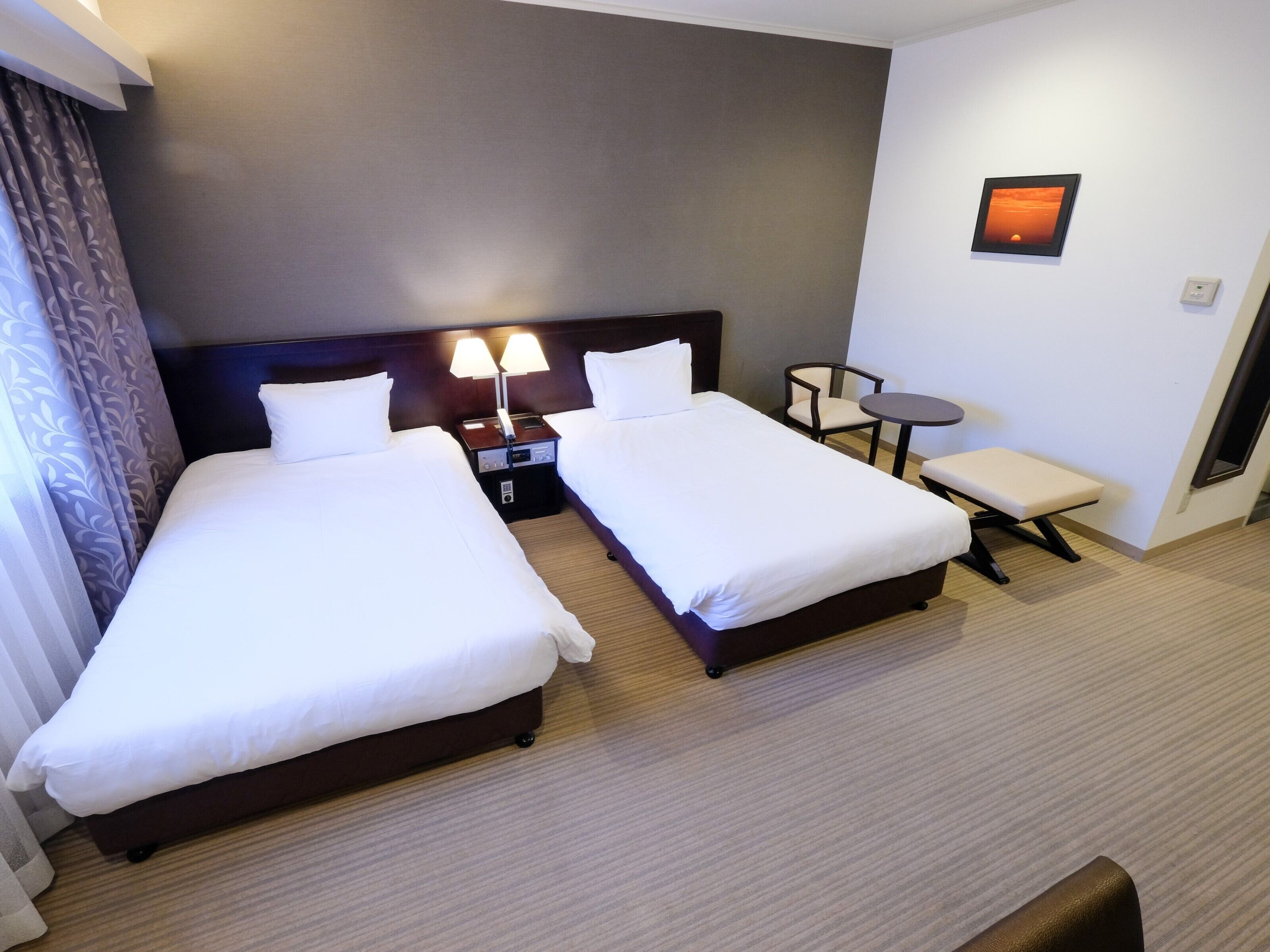 Habitación de hotel con dos camas individuales, una mesita, una silla y un banco.