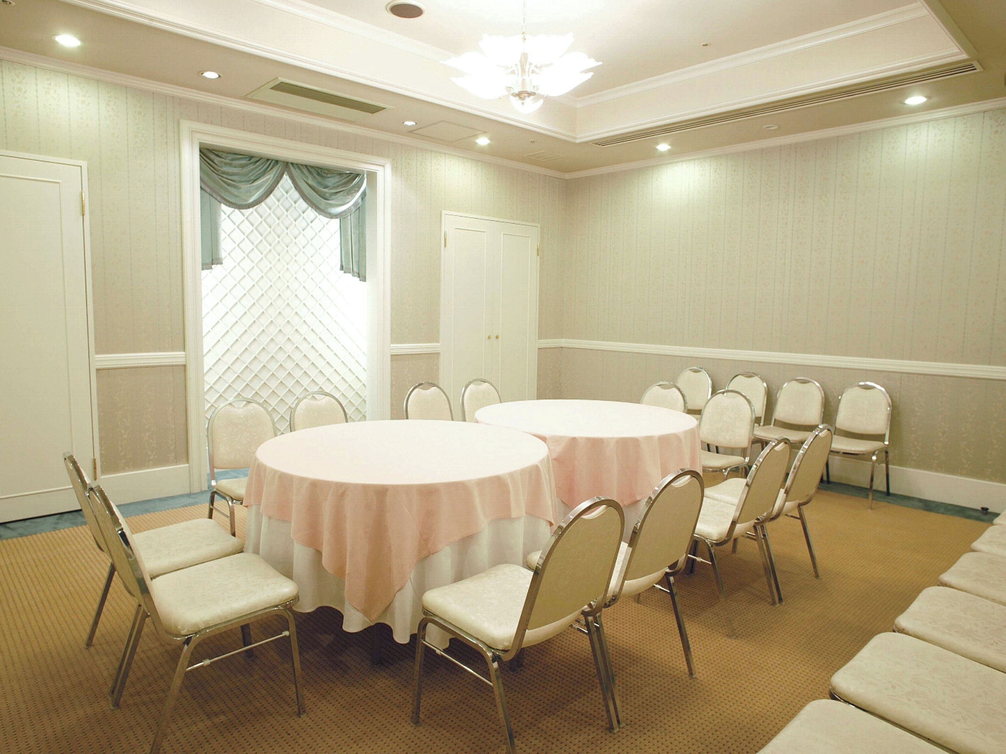A conference room with two round tables, beige chairs, and a patterned carpet.