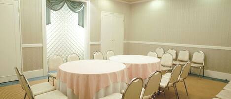 A conference room with two round tables, beige chairs, and a patterned carpet.
