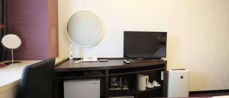 A hotel room with a bed, a desk with a computer, a television, a mini-fridge, a mirror, and a coffee maker.