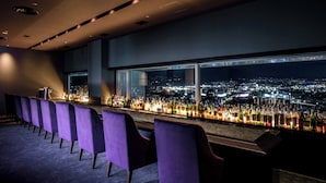 A bar with purple chairs and a city view at night.